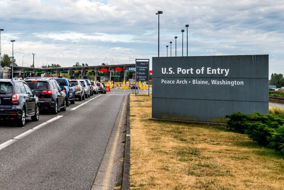 Cars line up at a U.S. port of entry near Peace Arch in Blaine, Washington, with a large entry sign on the right.