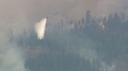Helicopter dumping water over a smoky forest fire on a hillside.