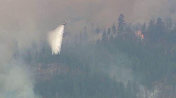 Helicopter dumping water over a smoky forest fire on a hillside.