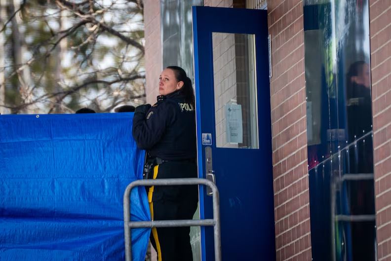 RCMP | Наш Ванкувер Police officer standing at a blue door beside a blue barricade outside a brick building, looking back over their shoulder.