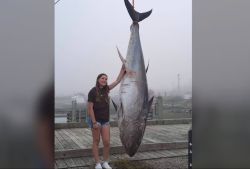 Young girl posing beside a massive suspended tuna on a dock, smiling at the camera.