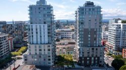 Aerial view of two tall modern apartment towers flanking a central low-rise building in a city neighborhood.",