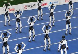 Group of white and black humanoid robots on a blue sports court performing synchronized arm poses.