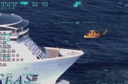 Large white ocean liner at sea with a small orange rescue helicopter near its bow.