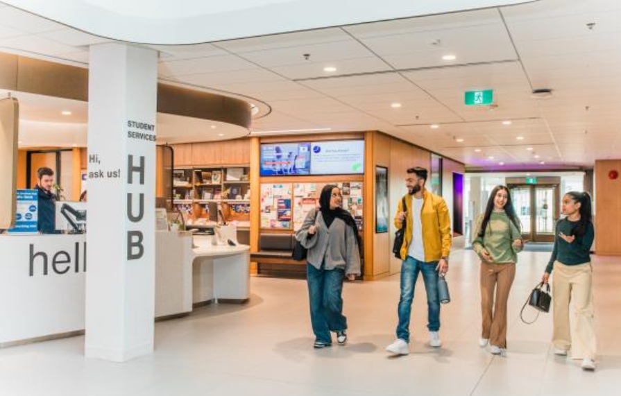 Group of students walking through a modern university lobby past the front desk in the student services area (Hub).