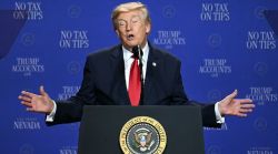 Man in a dark suit and red tie speaks from a podium with the presidential seal, arms outstretched, against a blue backdrop reading No Tax on Tips.