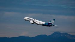 WestJet aircraft taking off with blue sky and mountain range in the background