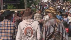 Two people in cowboy hats walk through a crowded outdoor event; one has a jacket that says 'Meet Me in the Desert.'