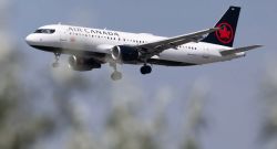 Air Canada passenger jet with gear down during approach against a blue sky with blurred foreground trees.
