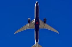 Bottom-up view of a dark blue commercial airplane flying overhead against a clear blue sky.