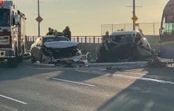 Emergency responders and a fire truck at the scene of a multi-vehicle crash on a bridge, with two heavily damaged cars and debris on the roadway.