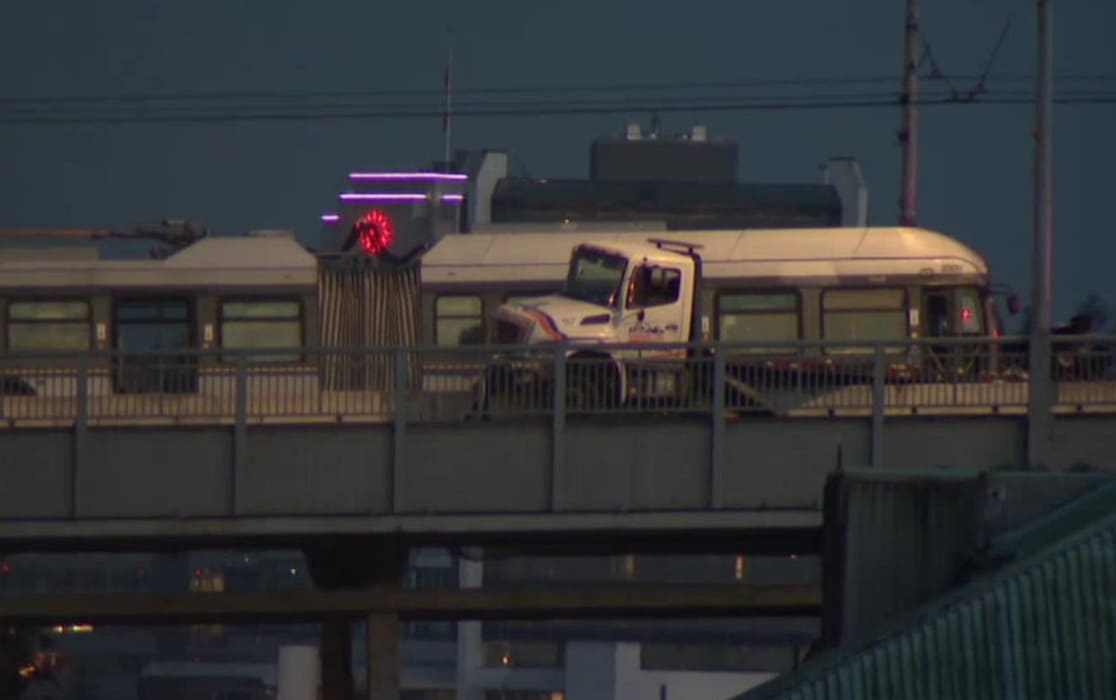 авария на мосту | Наш Ванкувер White tow truck on an elevated road beside a parked beige bus during dusk, city skyline in the background.