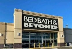 Exterior of a Bed Bath & Beyond store with a large black sign reading 'BED BATH & BEYOND' above glass doors on a beige facade.