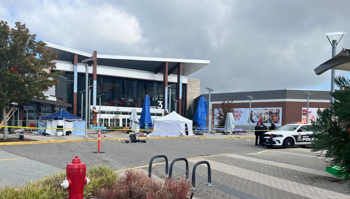 Shopping plaza exterior with police tape, tents, and a police car in a fenced-off area outside a store entrance.