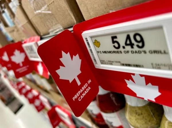 Red shelf tag with a white maple leaf and 'Prepared in Canada' text, placed next to a price display showing 5.49 in a store aisle.