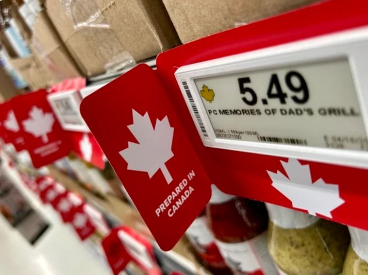 Red shelf tag with a white maple leaf and 'Prepared in Canada' text, placed next to a price display showing 5.49 in a store aisle.