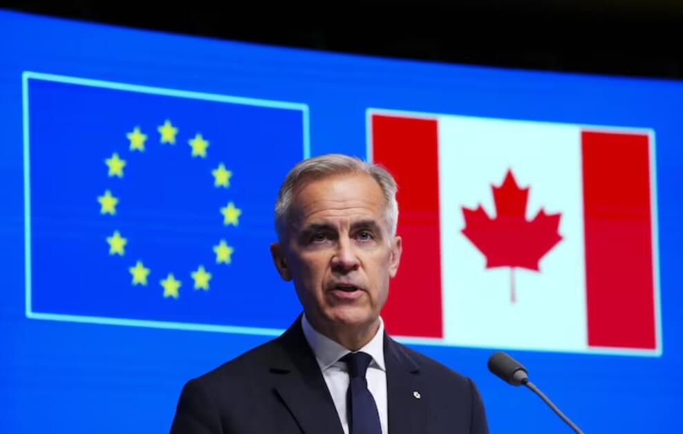 Speaker in a dark suit at a podium, with EU stars flag and Canadian flag behind on a blue backdrop.