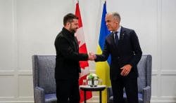 Two men in suits shake hands in a formal room with Canadian and Ukrainian flags behind them.