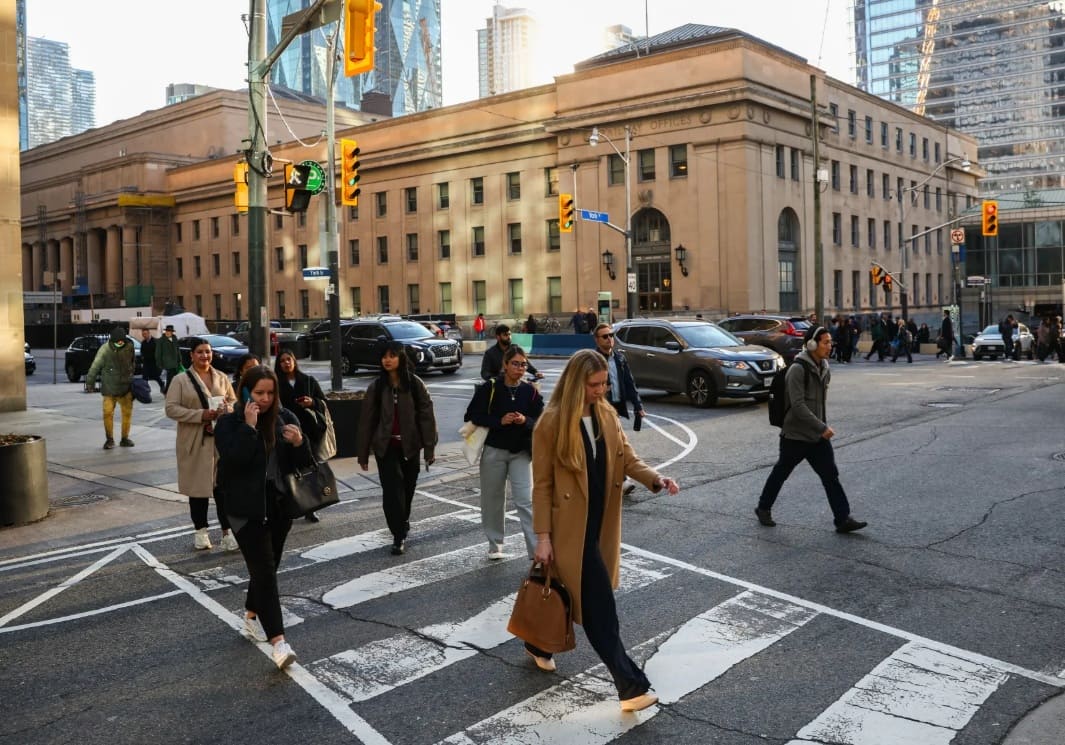 канада население снижение | Наш Ванкувер Group of pedestrians crossing a city street at a white-striped crosswalk in front of a beige historic building still in daylight.