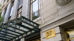 Concrete office building entrance with a glass canopy and a gold plaque beside the doorway.