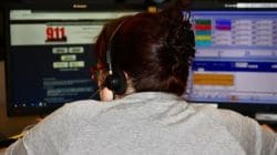 Back view of an operator wearing a headset at a dual-monitor dispatch desk, monitoring emergency software.