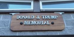 Wooden sign reading 'Donald J. Trump Memorial' mounted on a brick wall above a doorway.