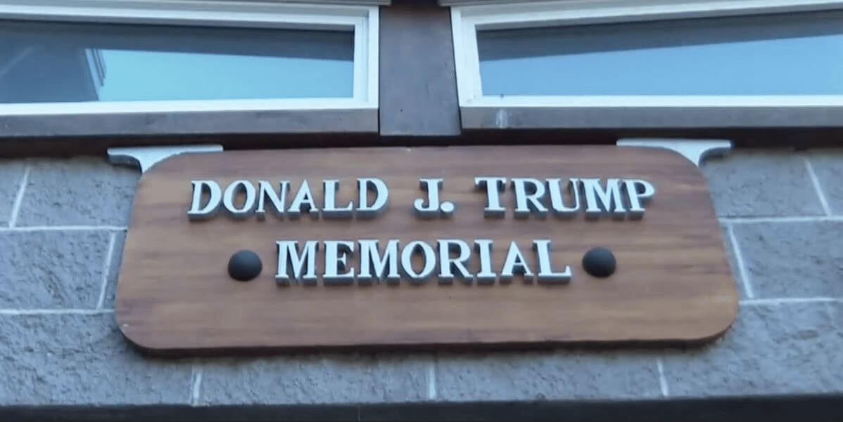 Wooden sign reading 'Donald J. Trump Memorial' mounted on a brick wall above a doorway.