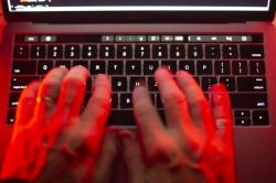 Hands typing on a backlit laptop keyboard with a red glow across the keys and screen edge visible.
