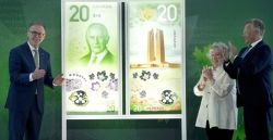 Three people in formal attire applaud beside a large display of redesigned Canadian $20 banknotes.