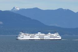 White BC Ferries passenger vessel sailing on calm blue water with forested mountains and snow-capped peaks in the distance