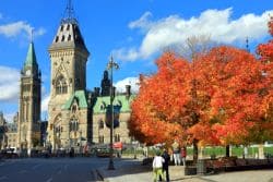 Parliament buildings with a bright blue sky and vibrant orange autumn trees in a city square.