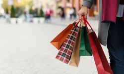 Person walking in a city street carrying several colorful shopping bags in one hand.