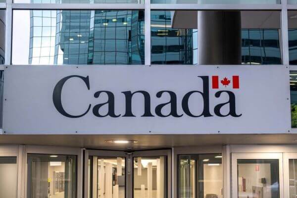 Exterior of a modern building with a large sign that reads 'Canada' and a small Canadian flag above, entry doors visible below.