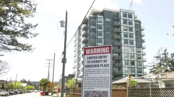 Construction site near a modern apartment building with a large WARNING sign about limited entry to Ridgeview Place in the foreground.
