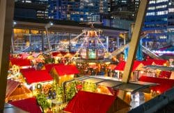 Nighttime city market with red-roof stalls, warm lights, and a central illuminated tower.