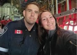 Two people taking a selfie inside a helicopter cockpit; man in uniform with a Canadian flag patch and a smiling woman beside him.
