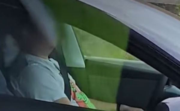 Person in a car wearing a seatbelt, seated in the front seat, holding a colorful object (green and pink) in their lap.