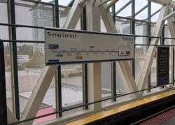 Sign reading Surrey Central with Platform 1 indicator and a transit map mounted on a railing inside a station interior.