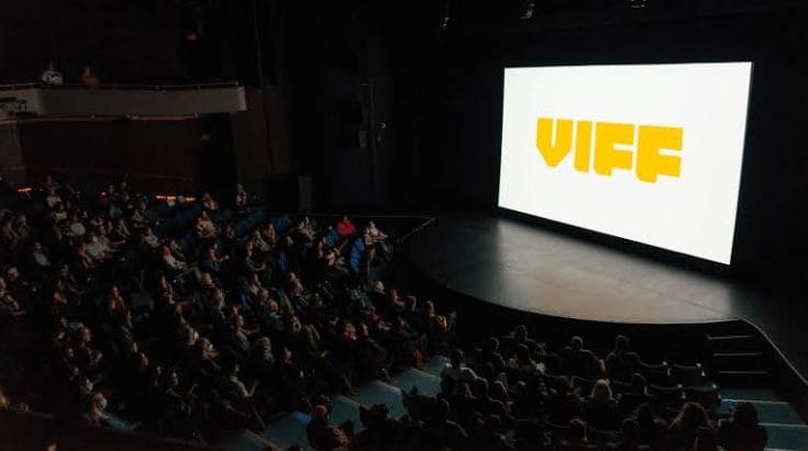 Dark theater with an audience watching a stage screen displaying 'VIFF' in bold yellow letters.