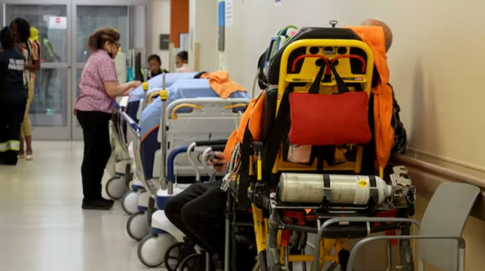 Hospital corridor with lined stretchers and medical staff tending to patients; orange emergency stretcher in the foreground.