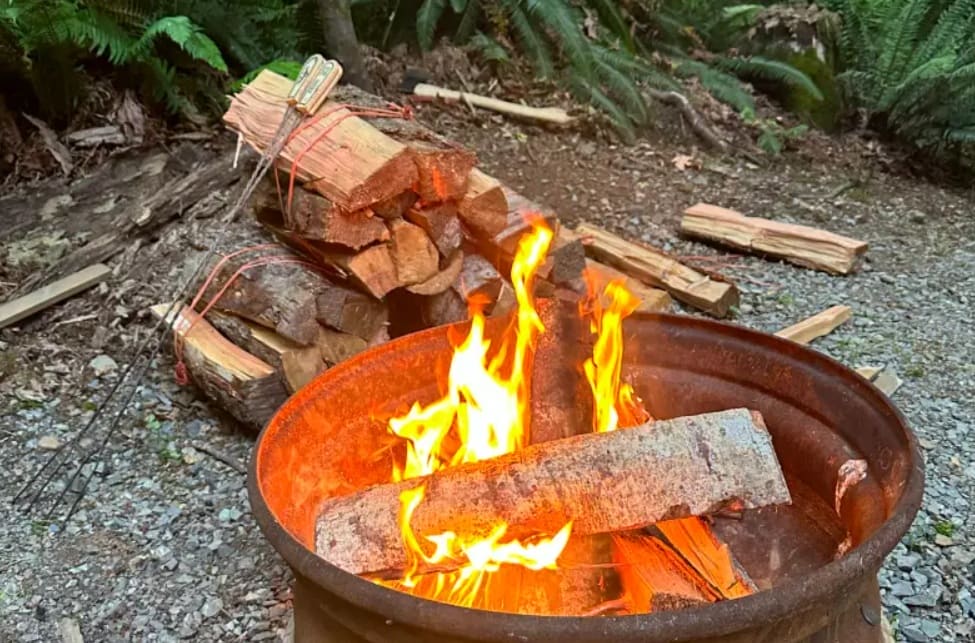 запрет на костры снят | Наш Ванкувер Blazing campfire in a round metal fire pit with split logs, outdoors on gravel.