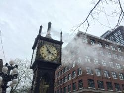 Часы Gastown Steam Clock на улице в Ванкувере днём, рядом прохожие и фасады старых зданий