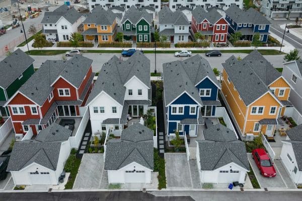 Aerial view of a suburban neighborhood with colorful two-story houses, driveways, and a street with cars to the side and across the row of homes missioned above.
