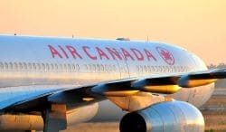 Air Canada passenger jet with red logo and lettering on white fuselage at sunset, wing and engine visible on the right side.