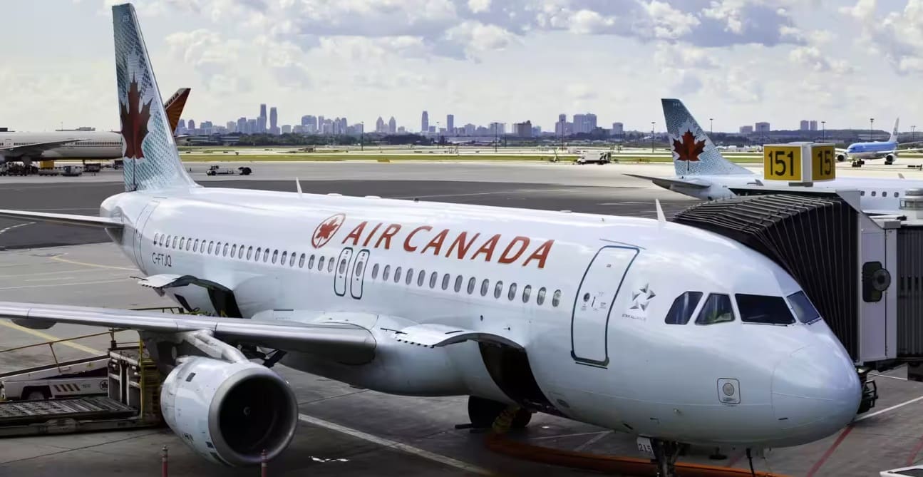 air canada отмена рейсов | Наш Ванкувер Air Canada airplane docked at a gate with a jet bridge, on the tarmac with a city skyline in the distance.