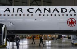 Air Canada airplane inside a hangar with people walking nearby, a maintenance setting visible around it.