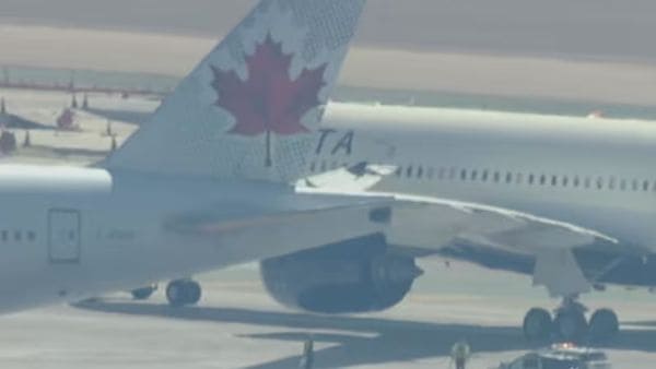 Air Canada aircraft tail with red maple leaf logo on a white fuselage, taxiing on the tarmac.