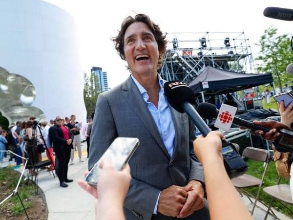Man in a gray suit being interviewed by reporters at an outdoor press event.
