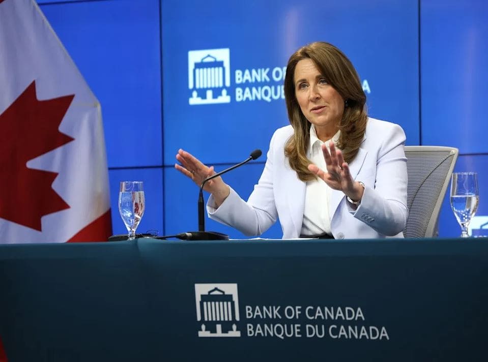 Woman in a light blazer speaks at a Bank of Canada press conference, with the Canadian flag in the background.