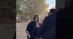 Woman in a denim jacket argues with a man in a dark hoodie in a parking lot during daytime.